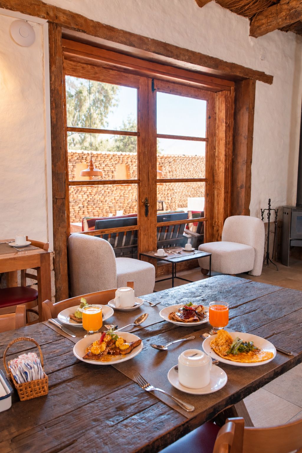Ein Essbereich mit Holztischen und -stühlen, ein Buffet mit Speisen und Getränken sowie ein Blick auf eine Terrasse im Freien mit einer Steinmauer und einer hängenden Leuchte.