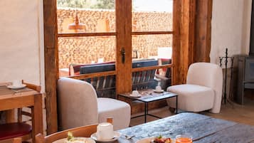 Ein Essbereich mit Holztischen und -stühlen, ein Buffet mit Speisen und Getränken sowie ein Blick auf eine Terrasse im Freien mit einer Steinmauer und einer hängenden Leuchte.