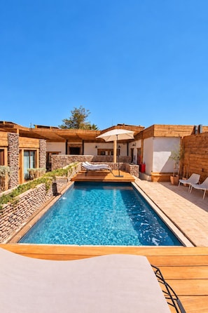 Un espace piscine doté d’une terrasse en bois, de chaises longues et d’un mur en pierre.