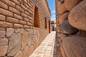 Un étroit sentier de pierre mène à un bâtiment doté d’une fenêtre en bois et d’un mur en pierre.
