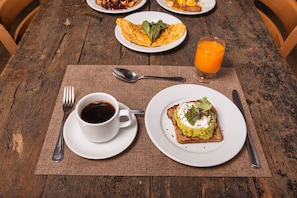 Ein Holztisch mit Frühstücksangeboten, darunter Toast mit Avocado, ein Spiegelei, eine Tasse Kaffee und ein Glas Orangensaft.