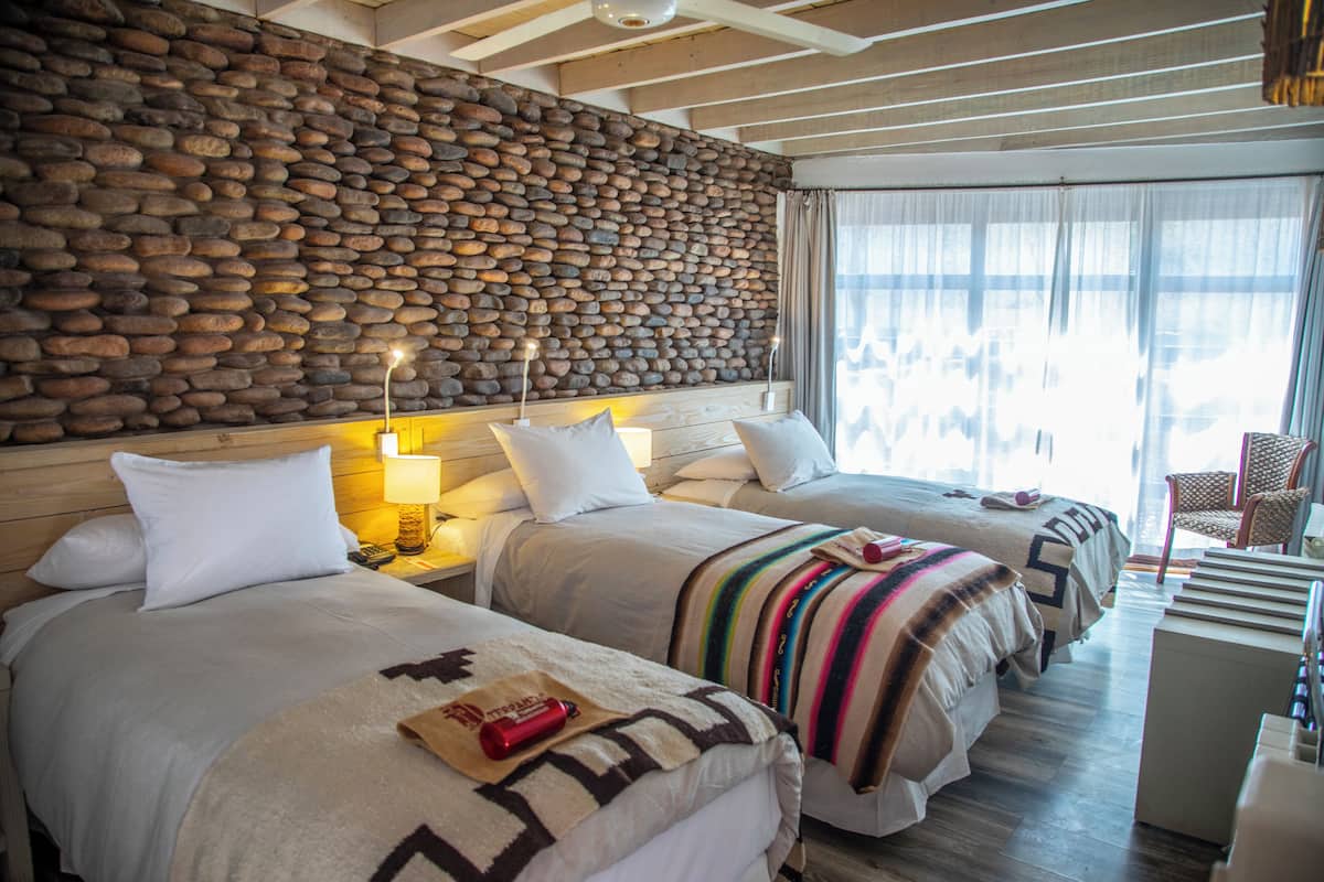 Ein Hotelzimmer mit zwei Betten, einer Steinwand, einer Holzbalkendecke und Blick ins Freie.