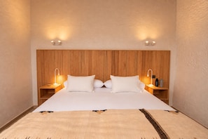 Une chambre d’hôtel avec un grand lit, une tête de lit en bois, deux tables de chevet avec des lampes et un luminaire fixé au mur.
