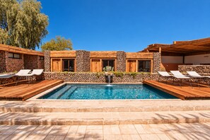 Ein Pool mit Holzterrasse und Liegestühlen, umgeben von Steinmauern und Holzfenstern.