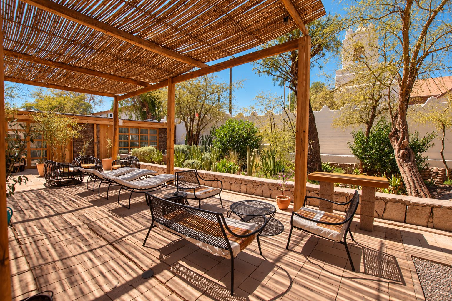 Un patio exterior con mobiliario de mimbre, una pérgola y vistas a un paisaje desértico.