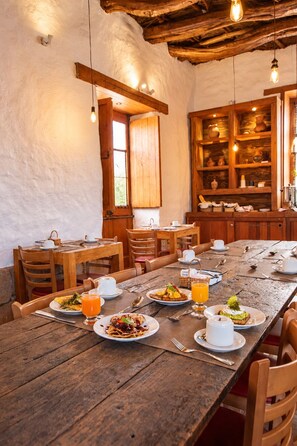 Ein rustikaler Essbereich mit Holztischen und -stühlen, einer großen Holzspeisekammer mit Geschirr und einer einfachen Holzbalkendecke.