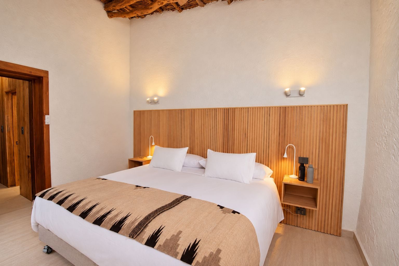 A hotel room with a wooden headboard, two bedside tables with lamps, a bed with white bedding, and a wooden floor.