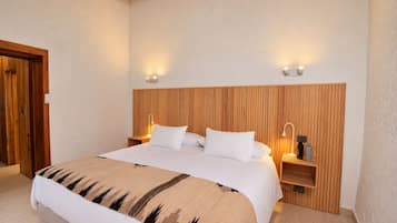 A hotel room with a wooden headboard, two bedside tables with lamps, a bed with white bedding, and a wooden floor.