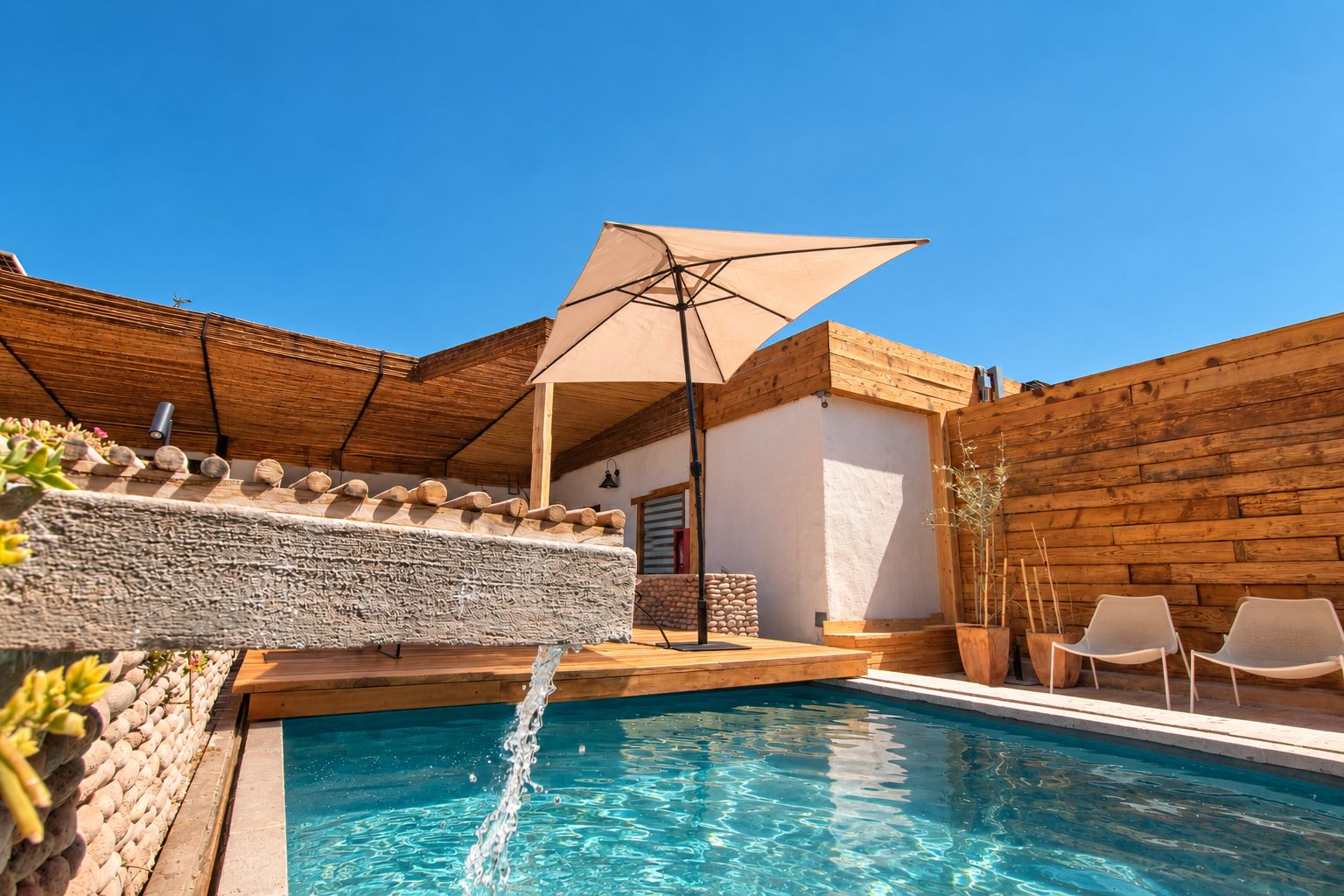Une piscine avec une terrasse en bois, un mur en pierre et une clôture en bois.