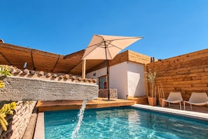 Une piscine avec une terrasse en bois, un mur en pierre et une clôture en bois.