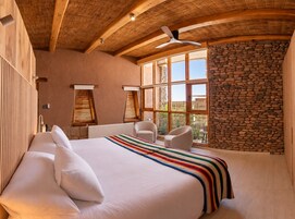Un dormitorio con una cama grande, dos mesitas de noche, un ventilador de techo y una pared de piedra.