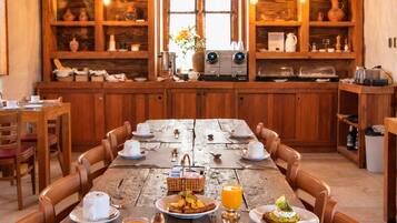 A rustic wooden dining area with a long table set for breakfast, surrounded by wooden cabinets with shelves.