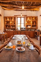 Un comedor rústico de madera con una mesa larga dispuesta para el desayuno, rodeado de armarios de madera con estantes.