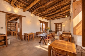 Ein rustikales Interieur mit Holztischen und -stühlen, einem reetgedeckten Dach und Steinwänden.