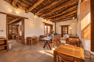 Un interior rústico con mesas y sillas de madera, techo de paja y paredes de piedra.