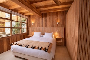 Une chambre à coucher en bois, avec un grand lit, deux tables de chevet avec des lampes et une fenêtre donnant sur un paysage verdoyant.