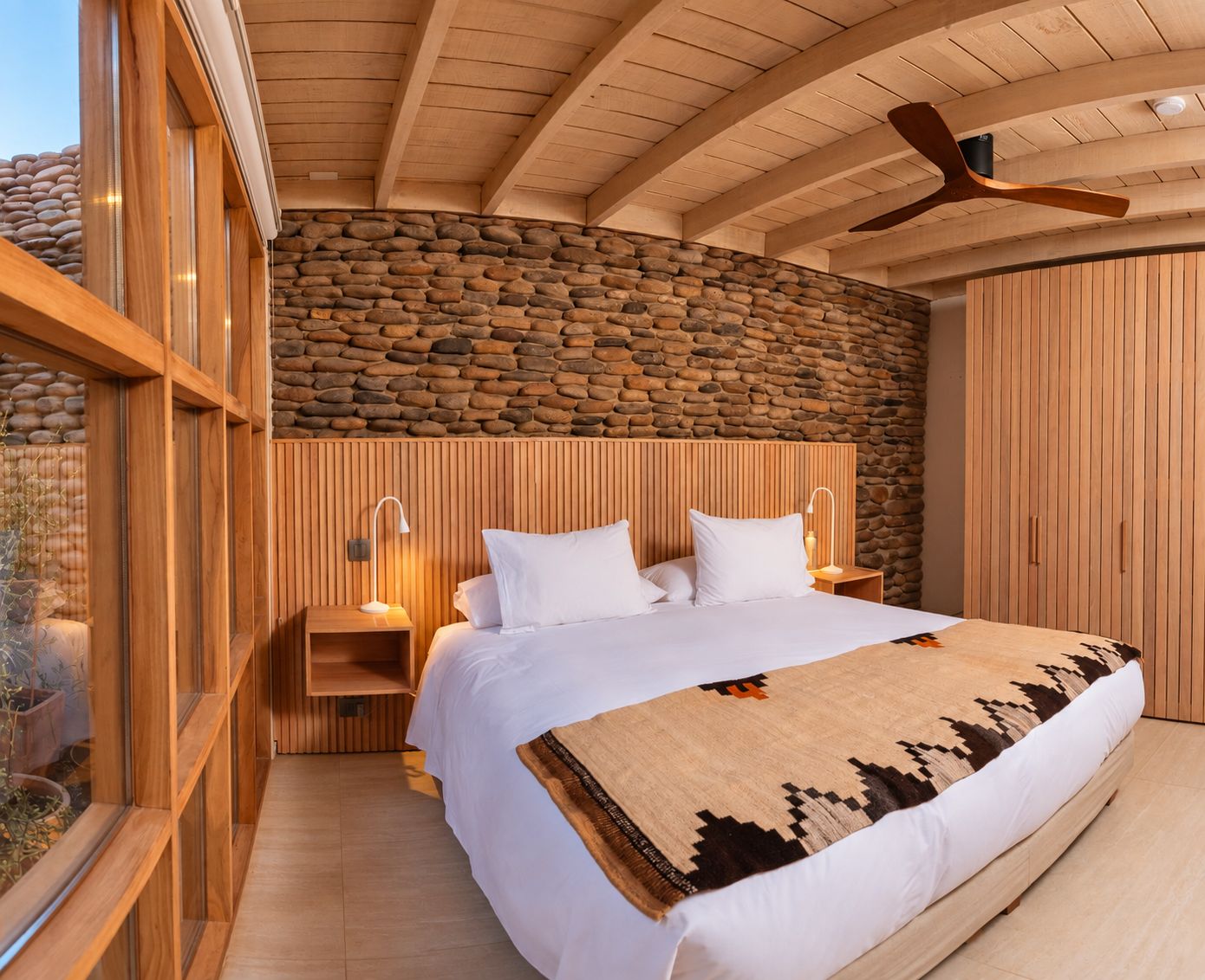 Quarto com parede de pedra, teto de madeira e cama com roupa de cama branca.