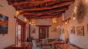 Un coin repas rustique avec des tables et des chaises en bois, un espace salon central avec un banc, et un plafond recouvert de chaume.
