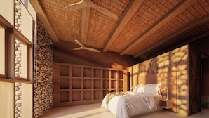 Une chambre à coucher avec un lit, une tête de lit en bois, un mur en pierre et un ventilateur de plafond.