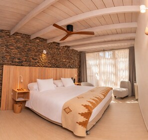 Een slaapkamer met een groot bed, houten hoofdbord, stenen muur en een plafondventilator.