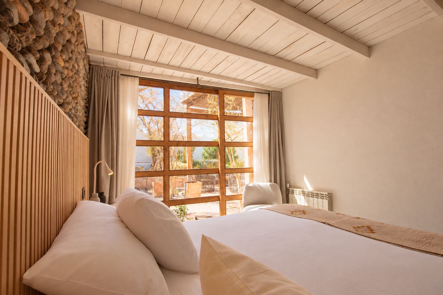 Une chambre avec une grande fenêtre, un plafond en bois et un lit avec des oreillers.