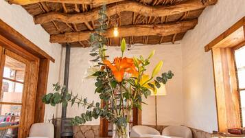 A rustic interior with a wooden table, chairs, a vase with flowers, and a thatched ceiling.
