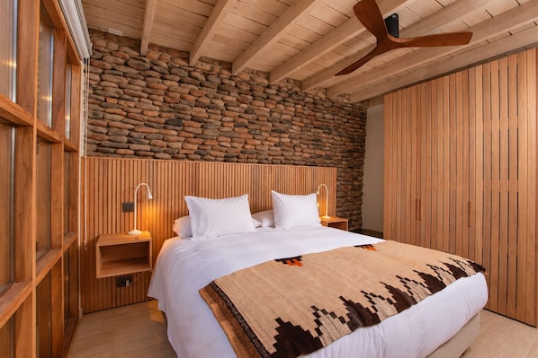 Ein Schlafzimmer mit Steinwand, Holzvertäfelung, einem Bett mit weißer Bettwäsche und einem Deckenventilator.