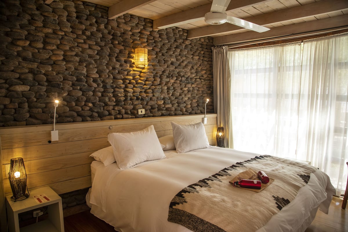 Ein Schlafzimmer mit Steinwand, Holz-Kopfteil und einem Bett mit wei ßer Bettwäsche.