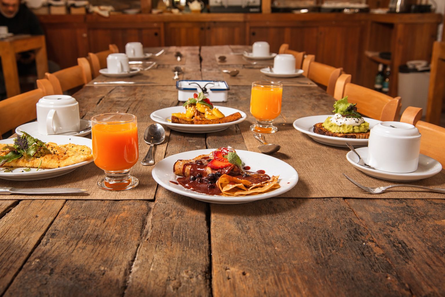 Una mesa de madera con varios platos de desayuno, como panqueques, gofres y una ensalada de frutas.