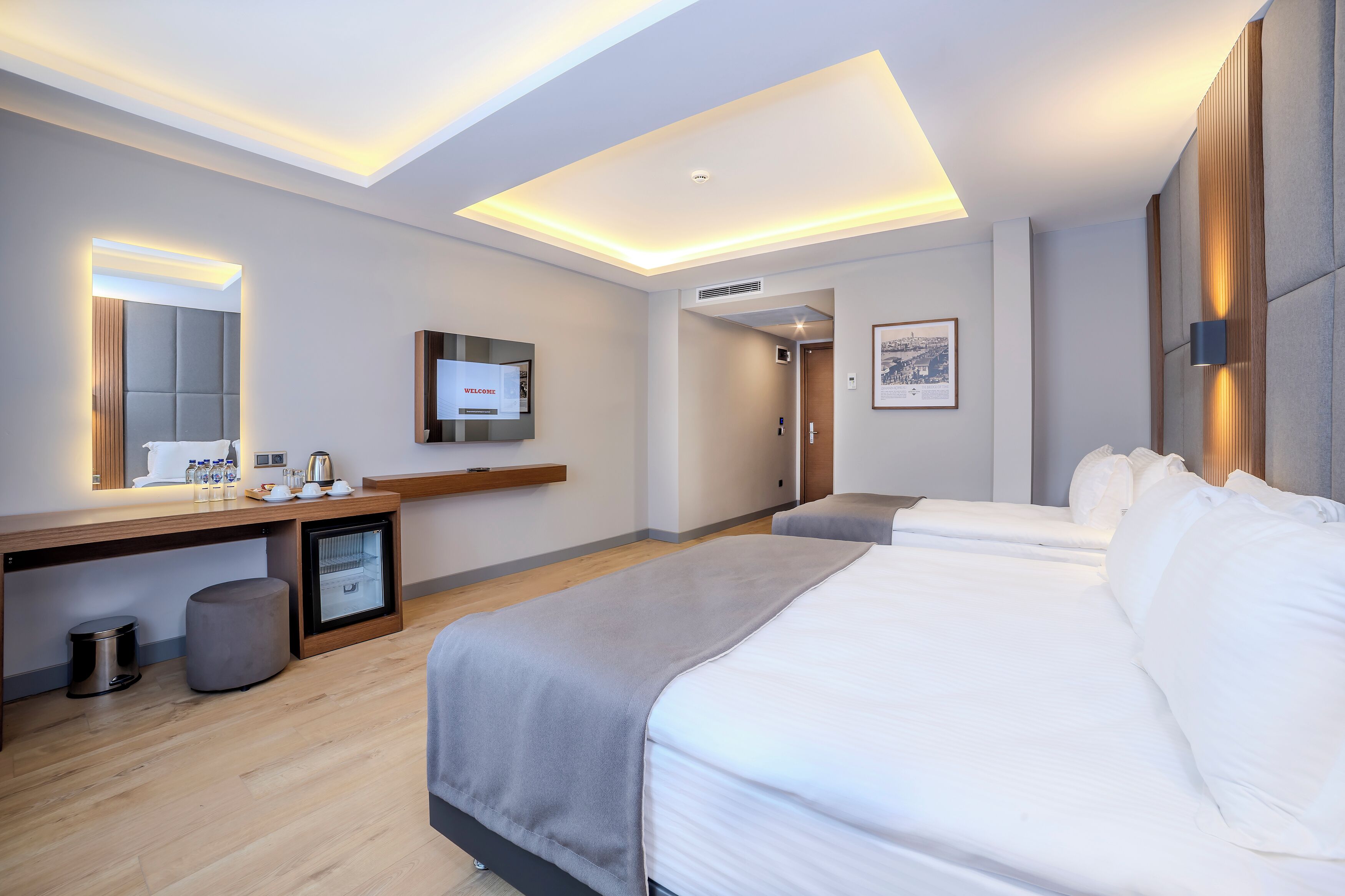 A modern hotel room with a large bed, a desk with a computer, a small seating area, and a large mirror.