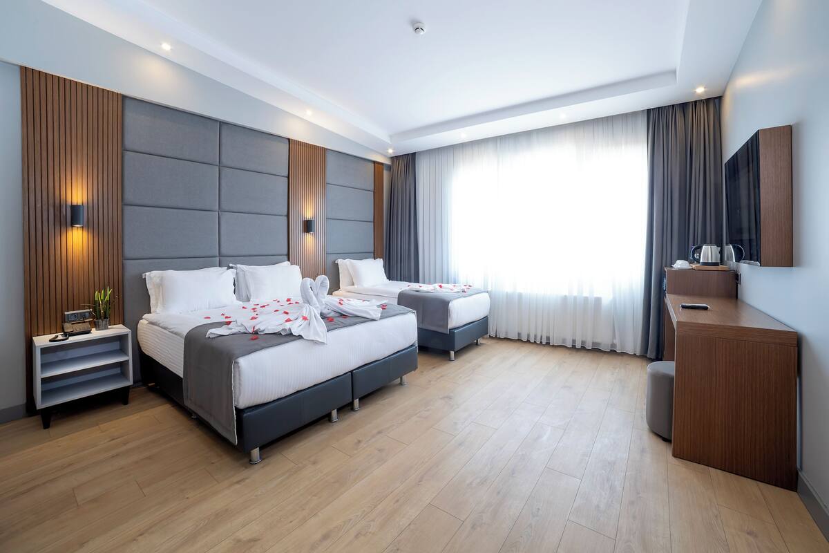 A modern hotel room with two beds, a desk, and a large window with curtains.