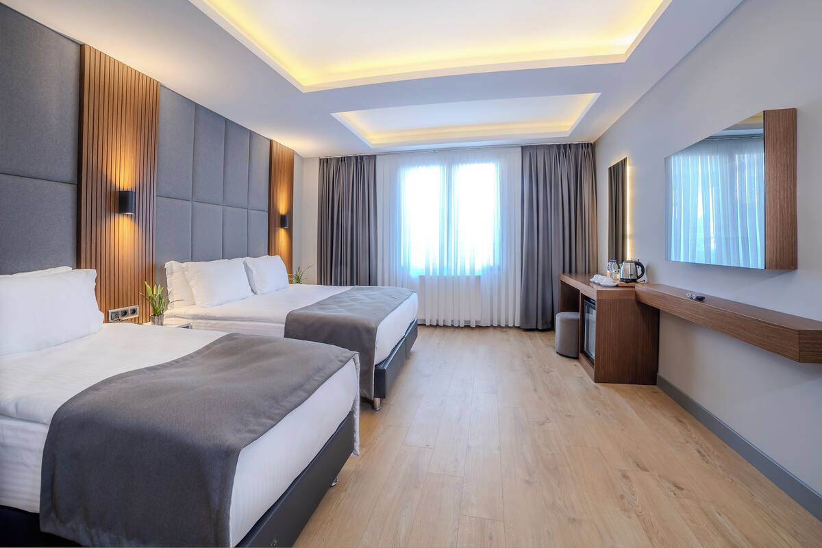 A hotel room with two beds, a desk, a mirror, and a large window with curtains.