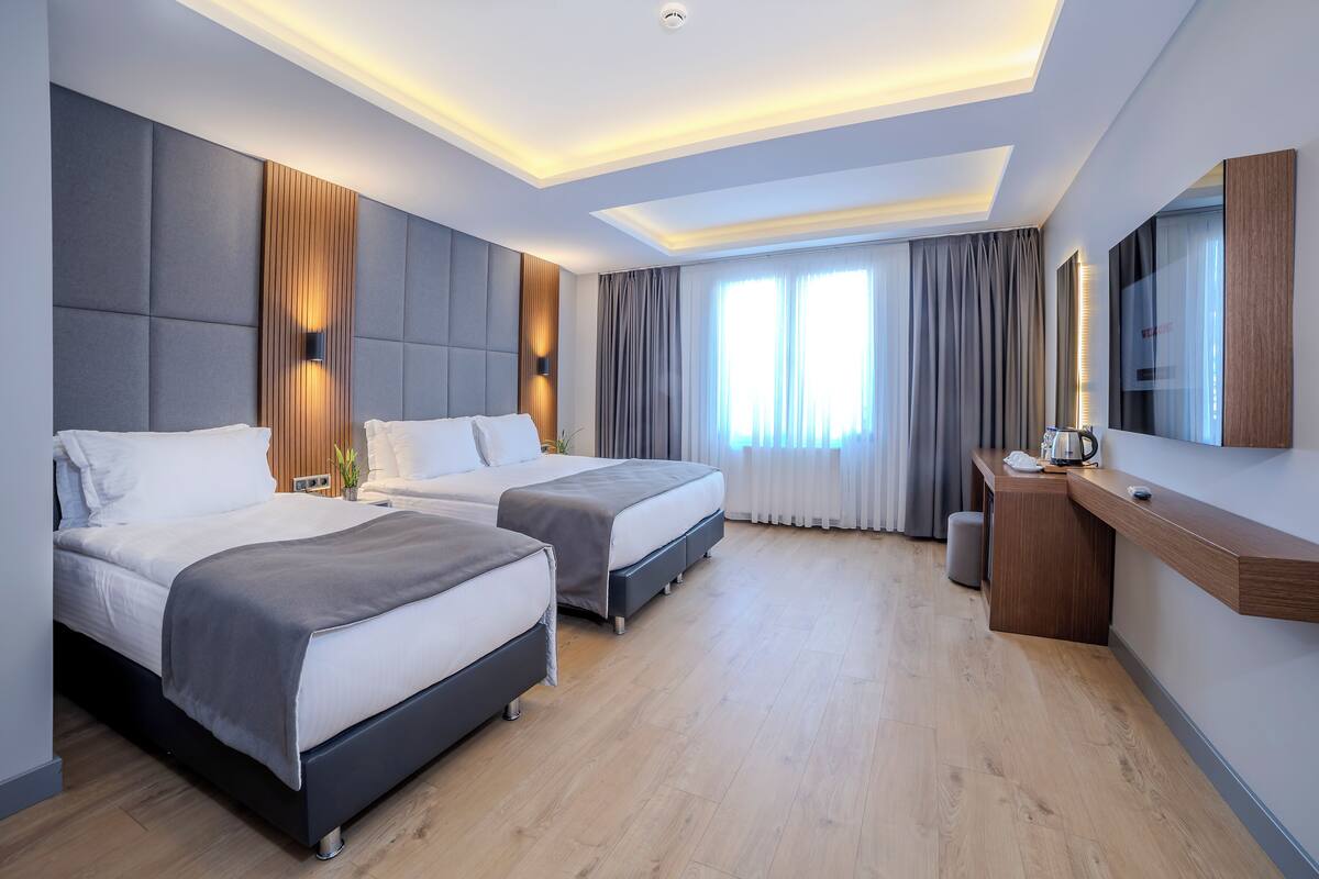 A modern hotel room with two beds, a desk, and a large window with curtains.