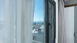 A room with a large window, a door, and a view of buildings and a body of water.