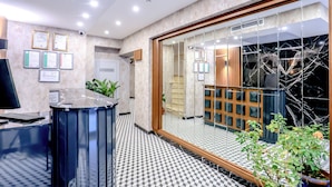 A reception area with a check-in counter, framed certificates on the wall, and a large glass door leading to a room with a wooden cabinet and a plant.