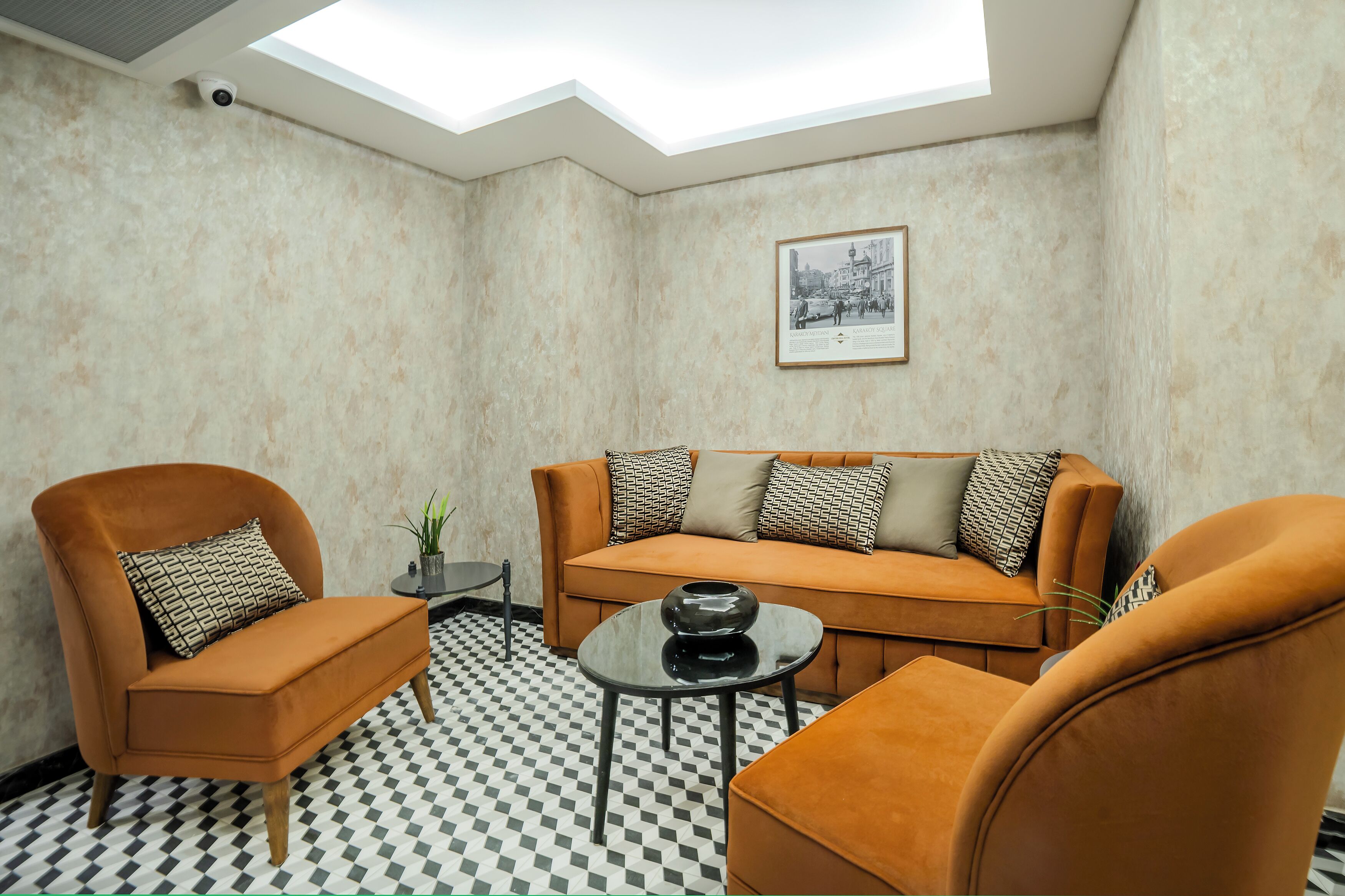 A room with a checkered floor, a sofa, two armchairs, a small table, a framed picture on the wall, and a skylight.