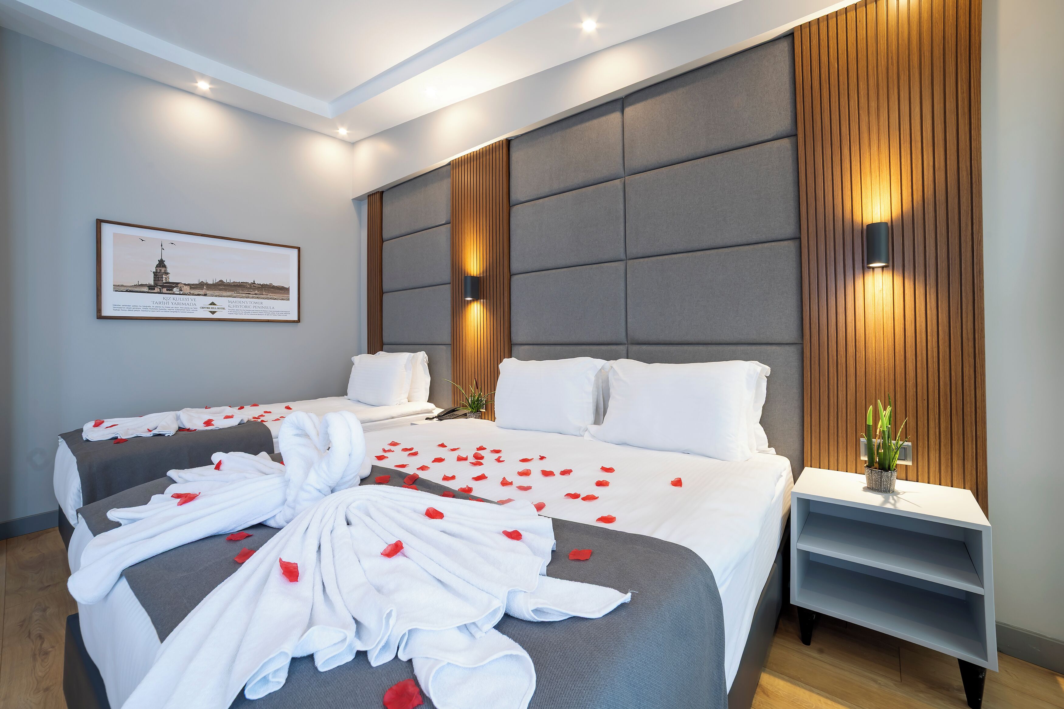 A modern hotel room with two beds, a large wall-mounted TV, and a framed picture on the wall.