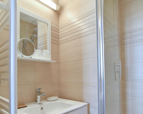 A modern bathroom with a glass shower enclosure, a white sink, and a mirror above it. - Hôtel Villa Sorel (Boulogne-Billancourt)