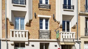 A multi-story residential building with balconies, a visible entrance, and a car parked in front. - Hôtel Villa Sorel (Boulogne-Billancourt)