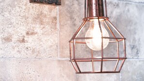 A wall-mounted light fixture with a vintage design, featuring a spool and a hanging bulb within a geometric metal frame. - Hôtel Villa Sorel (Boulogne-Billancourt)