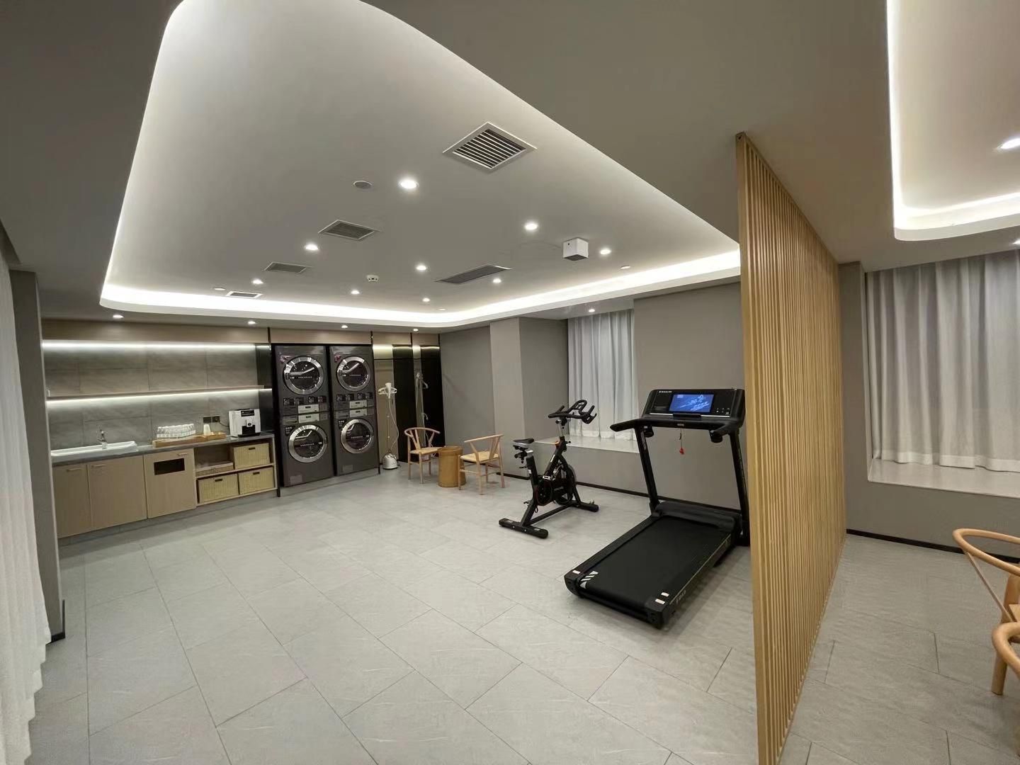 A modern hotel room with a kitchen, a treadmill, and a large window.