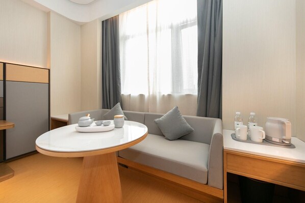 A modern hotel room with a round dining table, a sofa, and a small side table with amenities.