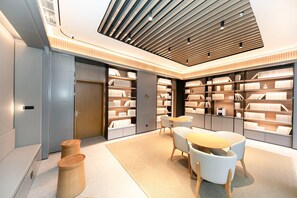 A modern library with bookshelves, a round table, and chairs. - Ji Hotel (Xi'an)