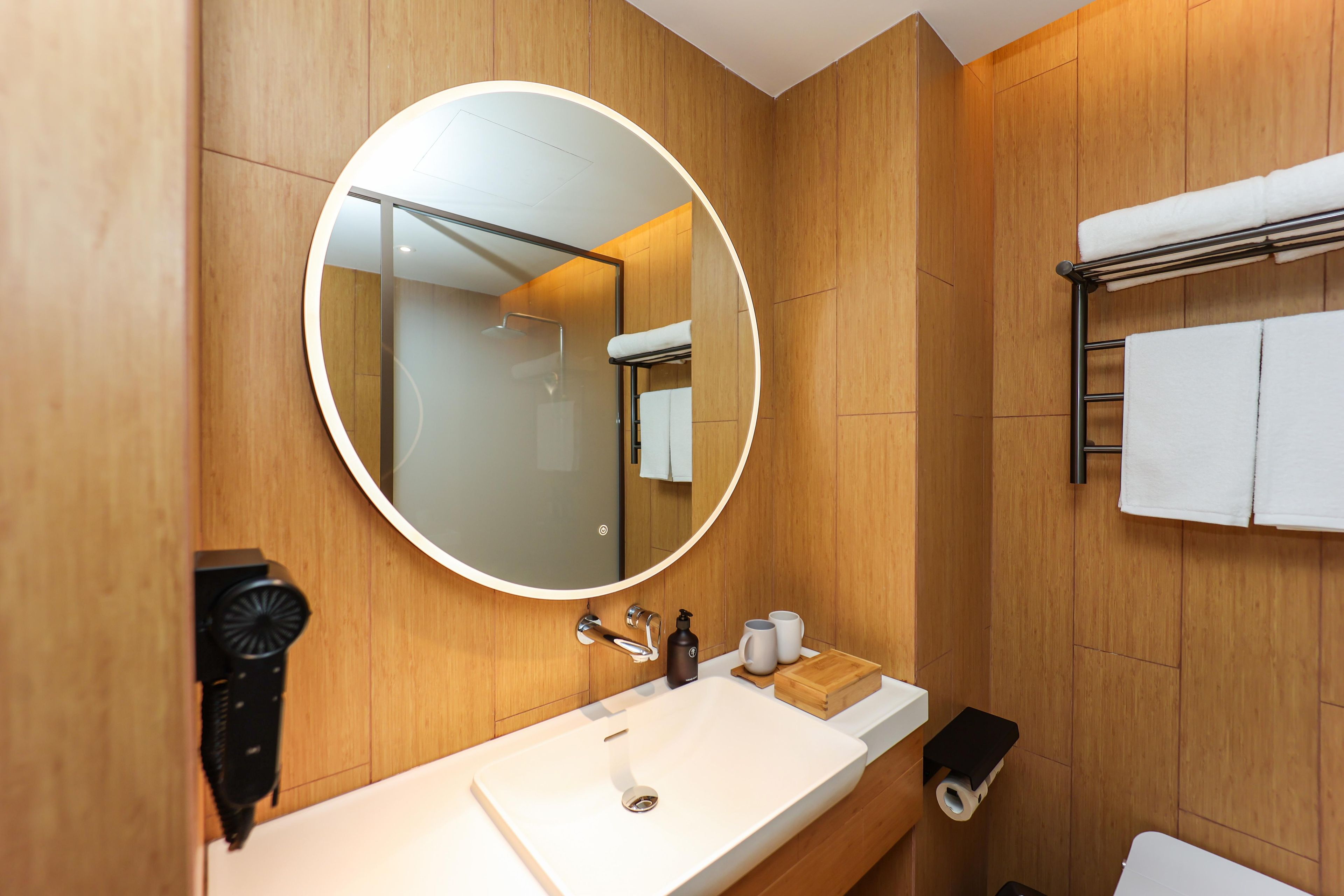 A modern bathroom with a round mirror, wooden paneling, a white sink, and a towel rack.