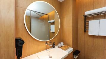 A modern bathroom with a round mirror, wooden paneling, a white sink, and a towel rack.