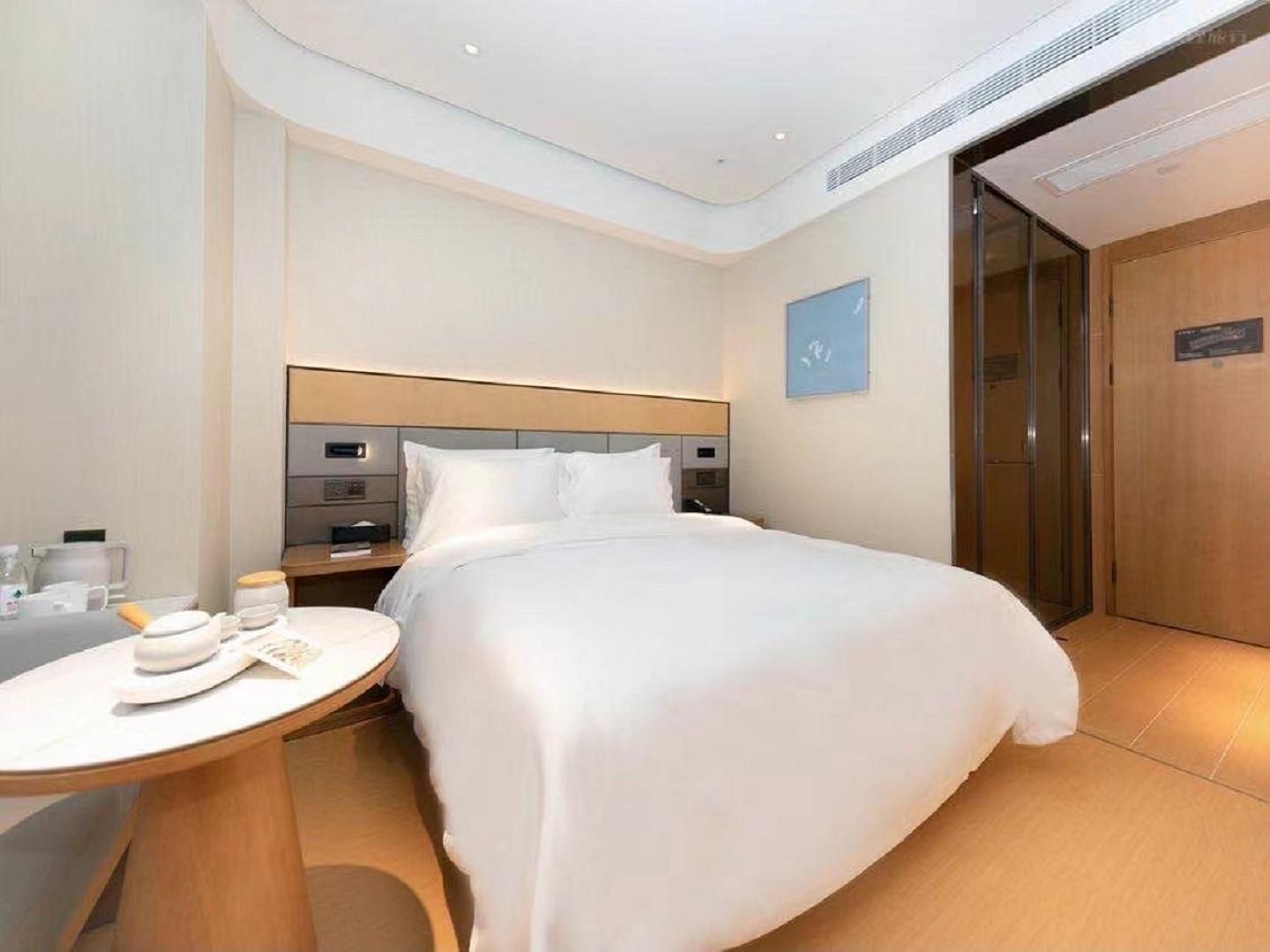A hotel room with a bed, bedside table, and a small round table with a hat and a book.