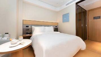 A hotel room with a bed, bedside table, and a small round table with a hat and a book.