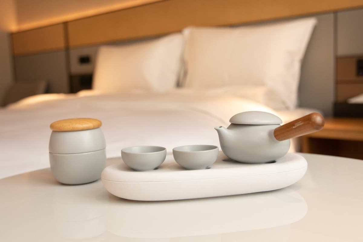 Un juego de té ordenado sobre una bandeja blanca en una habitación de hotel, con una cama al fondo.