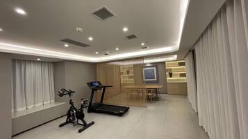 A modern gym with exercise equipment, a dining area, and a large window with curtains.