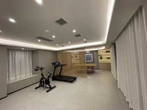 A modern gym with exercise equipment, a dining area, and a large window with curtains.